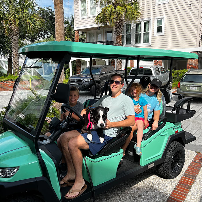 A Family with their dog enjoying their brand new Bintelli Beyond Lifted 6PR street legal golf cart in mint parked on their driveway.