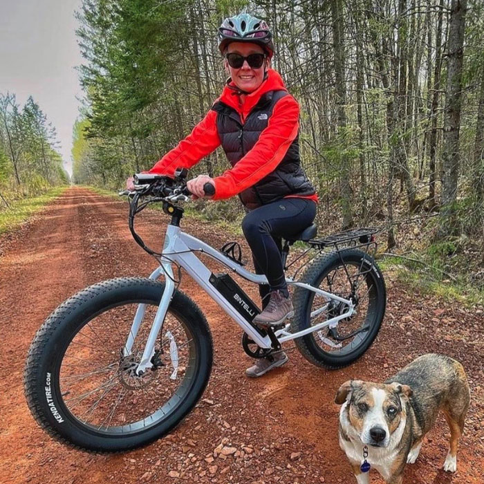 A man riding the bintelli electric bike down a dirt road next to a dog