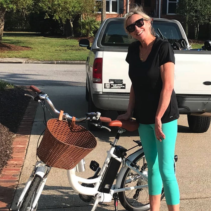 A woman standing next to the bintelli electric bike on a sidewalk in USA