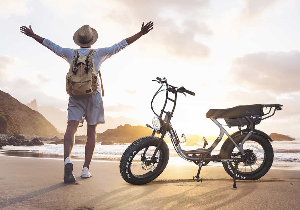 Man rode his Bitnelli electric bike to the ocean. He watches the sunset happily while his electric bike is parked next to him.